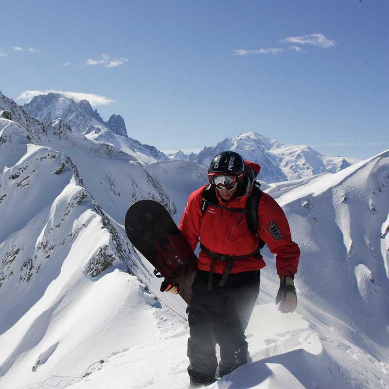 Person carrying a snowboard at the top of a mountain